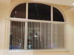 an image of Vertical blinds covering a large, arched window in a light-coloured room.