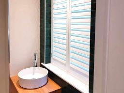 a picture of a Modern bathroom with a round sink on a wooden shutter and white louvres in the  window.