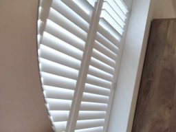 and image of White wooden shutters partially open on a window with a wooden floor.