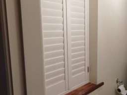 an image of closed White louvered shutters covering a window with a wooden ledge below.
