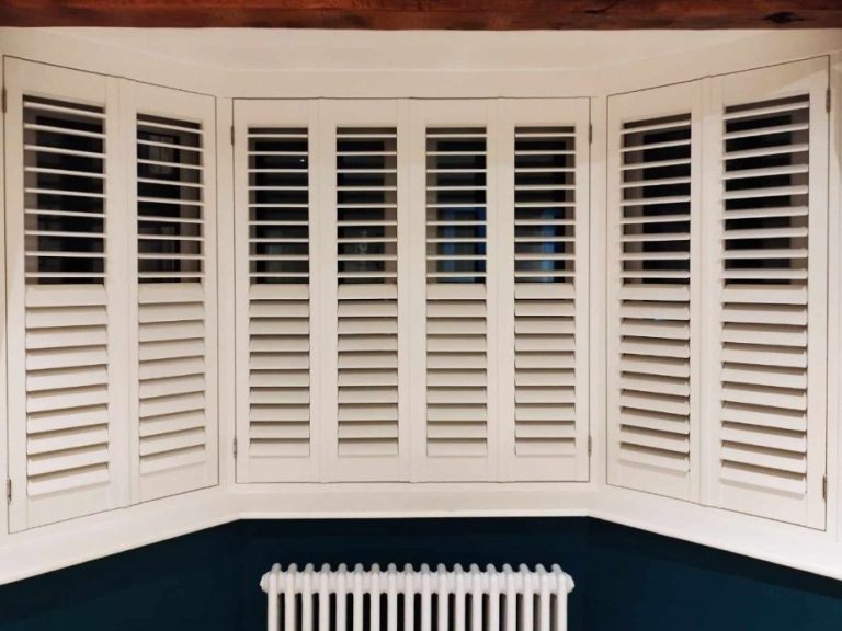 an image of White wooden shutters on a bay window with a radiator below.