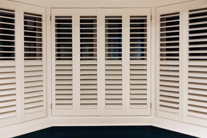 a picture of White wooden shutters in a bay window with white louvers.