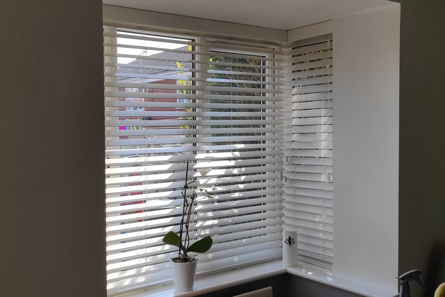 picture of a bay window with blinds. A corner window with white blinds and a small potted plant on the sill.