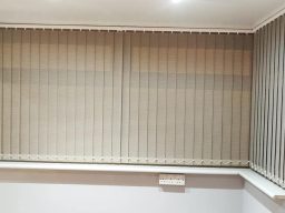 a picture of Vertical beige blinds covering a window with a light grey wall background.